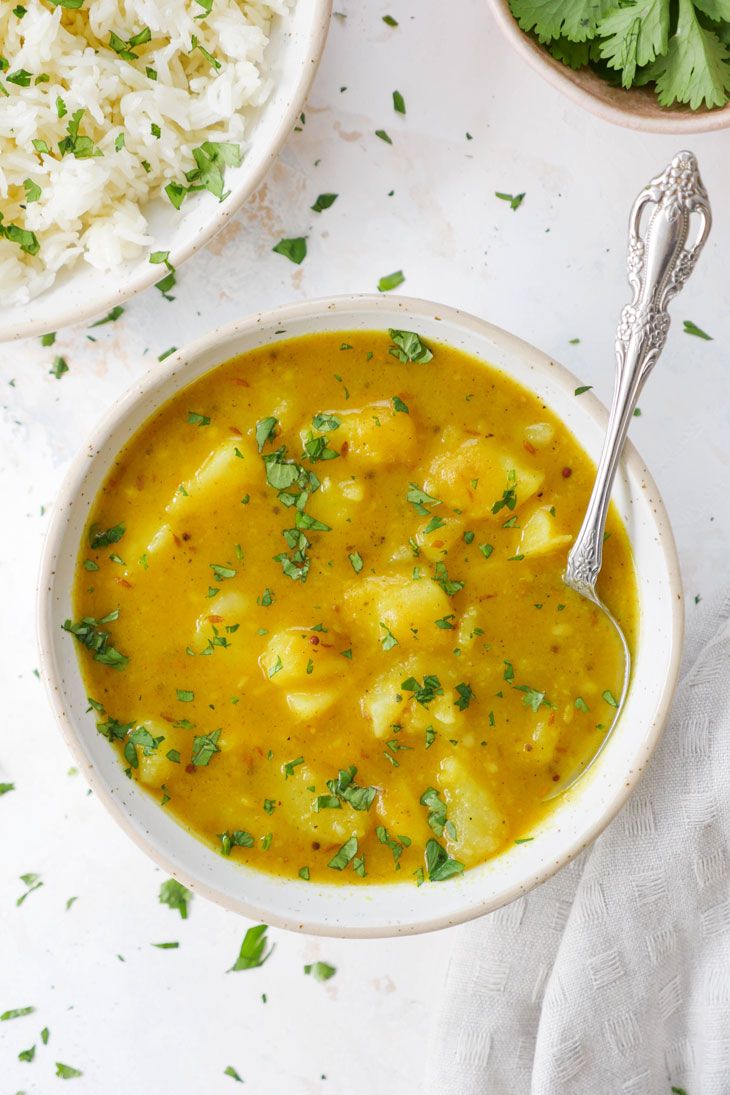 two bowls filled with curry and rice on top of a white tablecloth next to a spoon