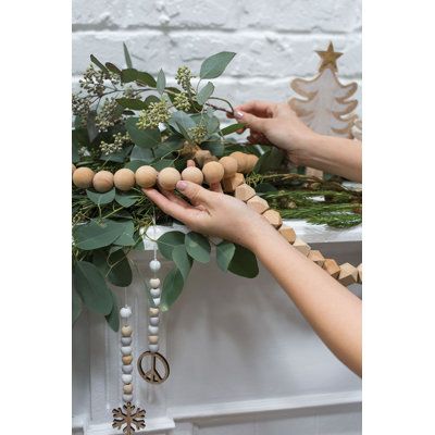 two hands are decorating a wooden beaded garland with greenery and peace signs