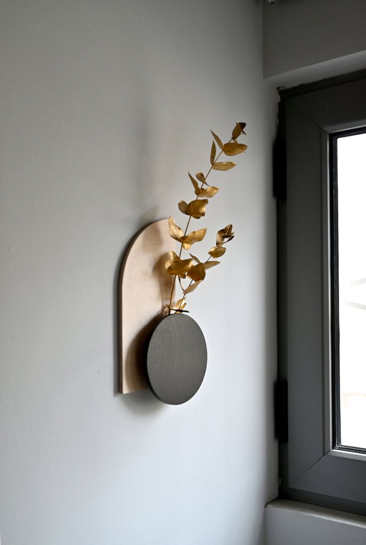 a wall mounted clock on the side of a white wall next to a vase with flowers in it