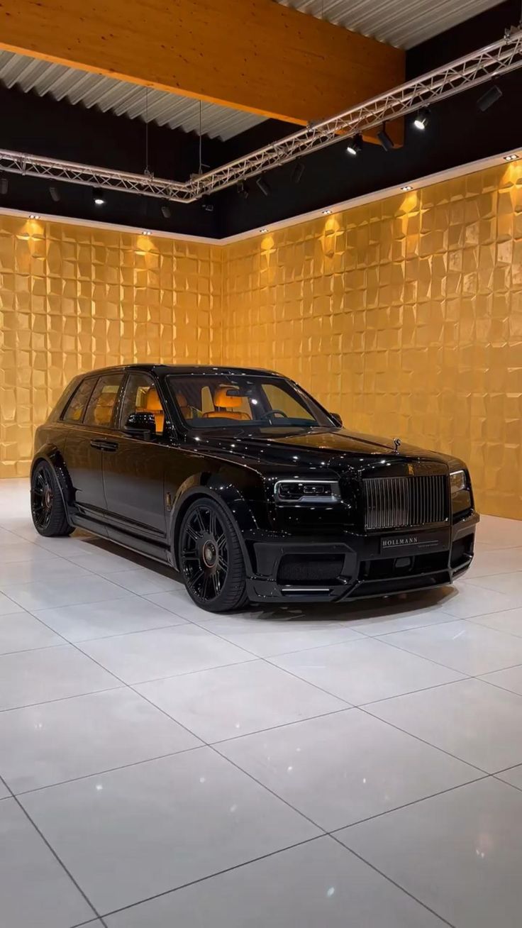 a black rolls royce parked in front of a gold wall