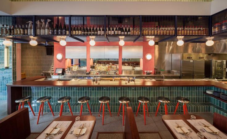 the interior of a restaurant with tables and stools in front of an open kitchen