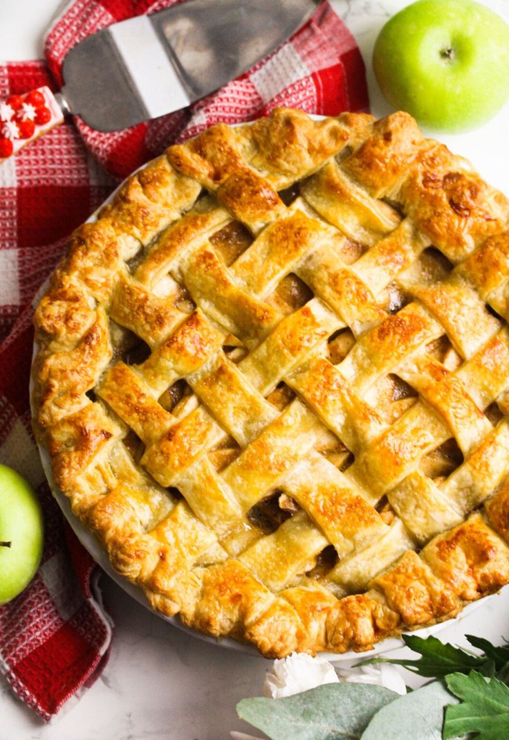 an apple pie sitting on top of a table next to two apples and a knife