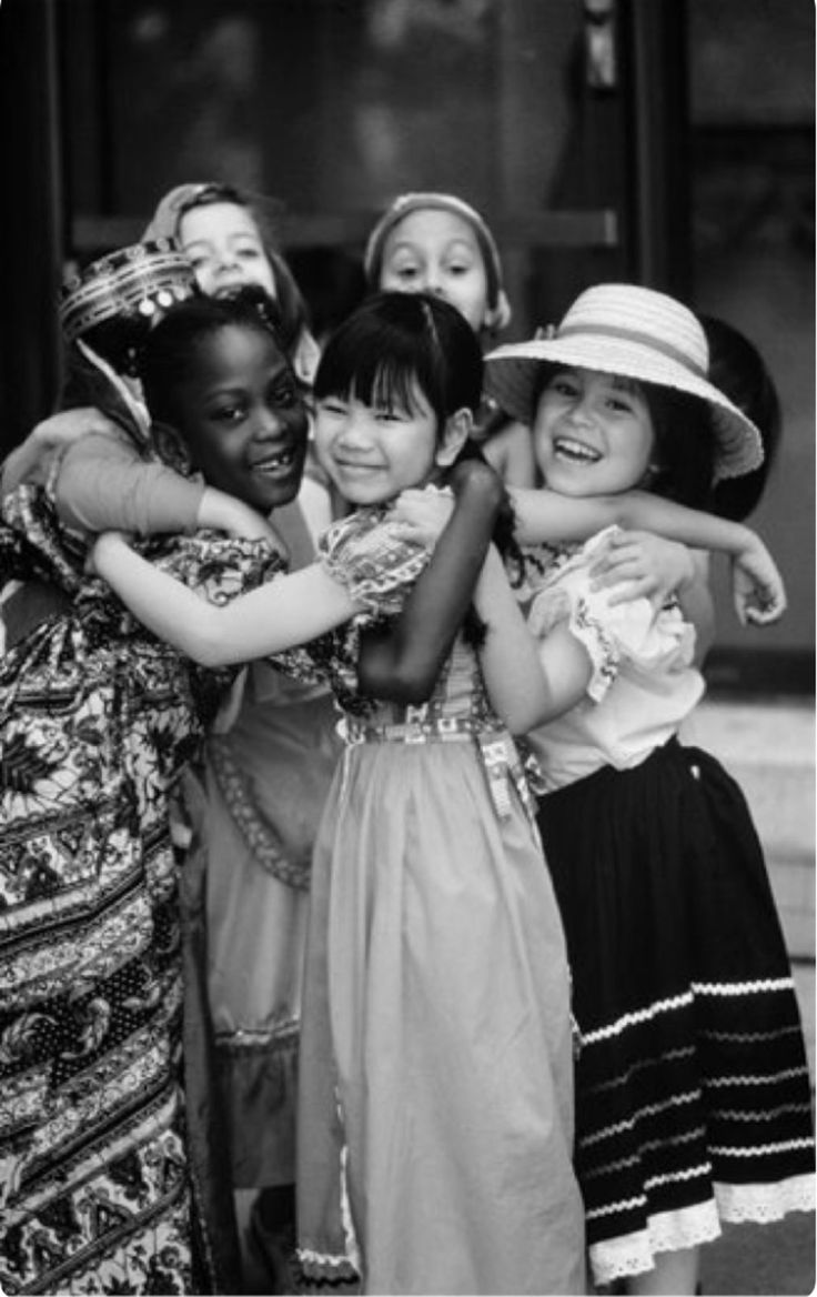 black and white photograph of four girls hugging each other with hats on their heads in front of a building