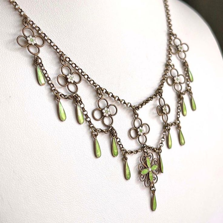 This antique silver and green and white enamel necklace was hand crated in the Arts and Crafts era, around 1910 by famed Norwegian silver smith Marius Hammer. Hammer lived from 1847-1927 and worked in Bergen, Norway. This drop necklace features flowers and drops of bright spring green and matte what enamel with that velvety look that Hammer was a master of. Chains of silver weave throughout this necklace, piecing together a lovely statement piece of swirls, loops, and twists. This piece weighs 10.3 grams and measures 16 inches in length. It has been acid tested. A mark on the back reads, ‘930S’, indicating fine silver and it bears the hallmark of the M with a hammer forming the center.  Wearable on a Saturday night date, give-able for a wedding present, presentable at a cocktail party, and Michael Michaud Necklace, Fae Necklace, Green Metal Collectible Jewelry, Victorian Enamel Pendant Jewelry, Necklace Styles, Art Deco Silver Jewelry With Vintage Charm, Regency Necklace, Victorian Round Enamel Jewelry, Silver Art Deco Jewelry With Vintage Charm