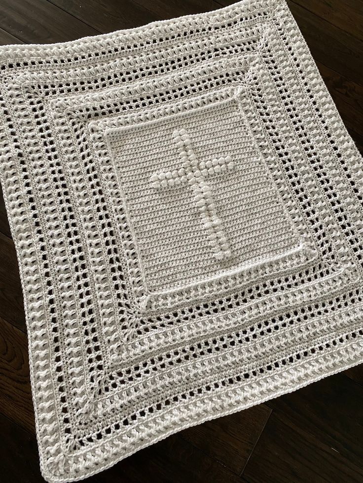 a white crocheted blanket with a cross on the front and center, sitting on top of a wooden floor