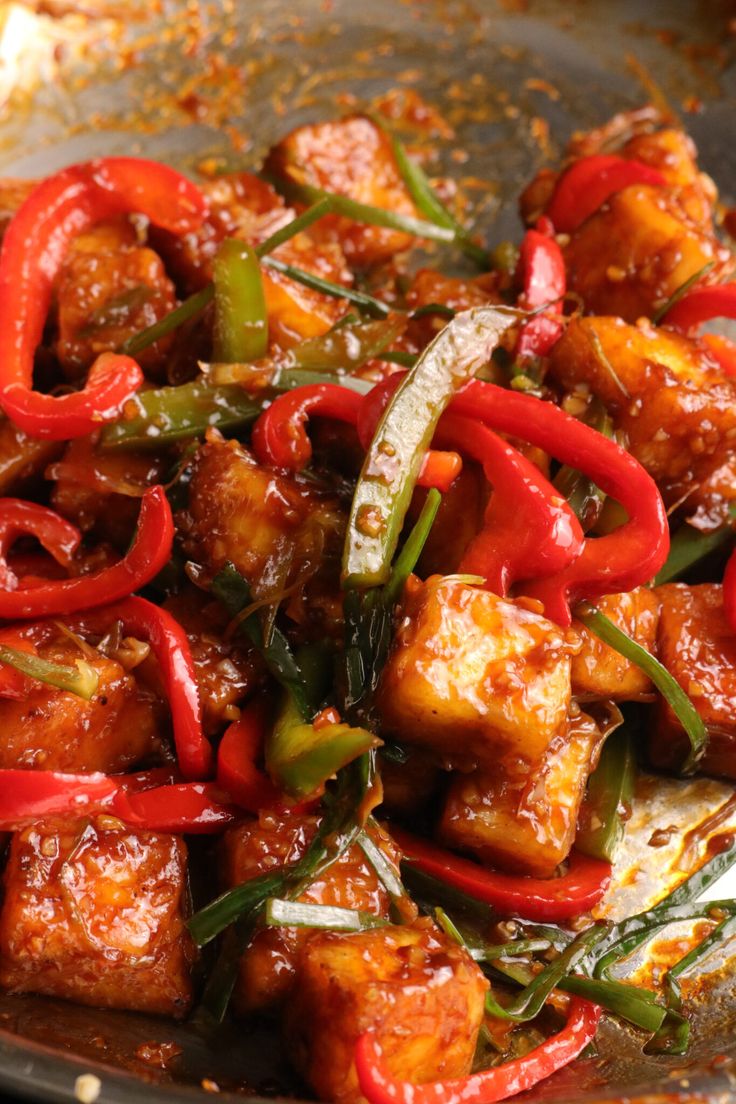 a pan filled with tofu and peppers on top of a wooden table next to other food items