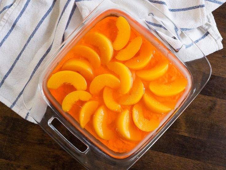 a glass dish filled with sliced peaches on top of a wooden table next to a blue and white towel