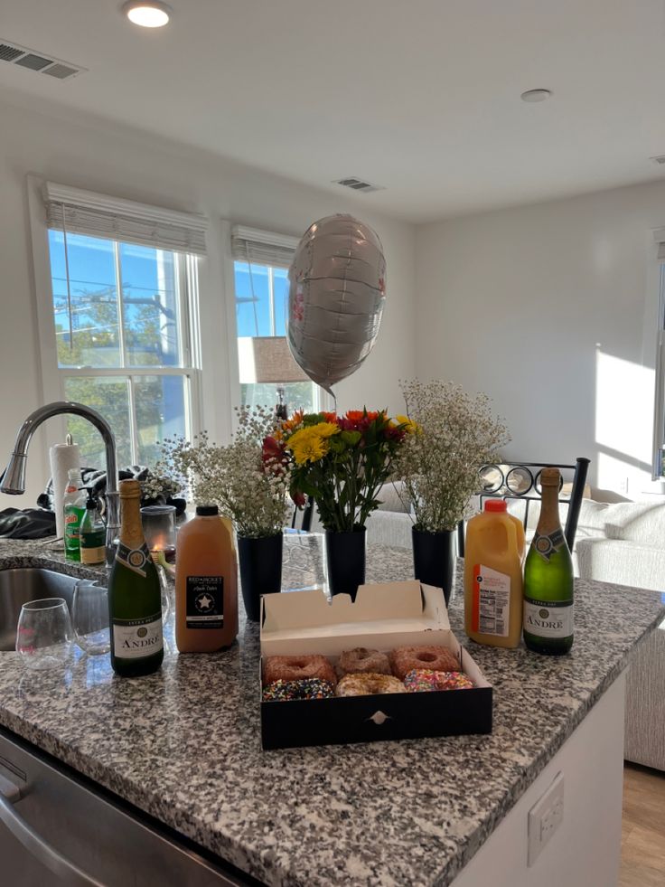 a kitchen counter topped with bottles of wine and food next to a vase filled with flowers