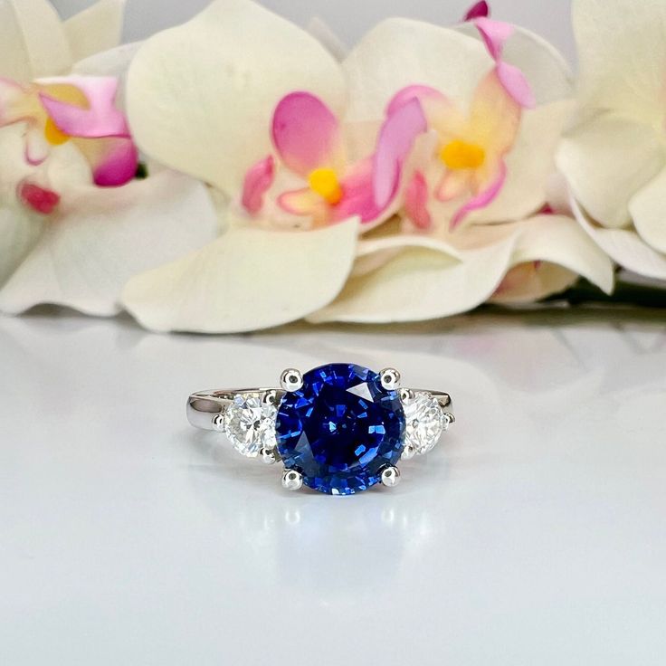 a blue and white diamond ring sitting on top of a table next to orchids