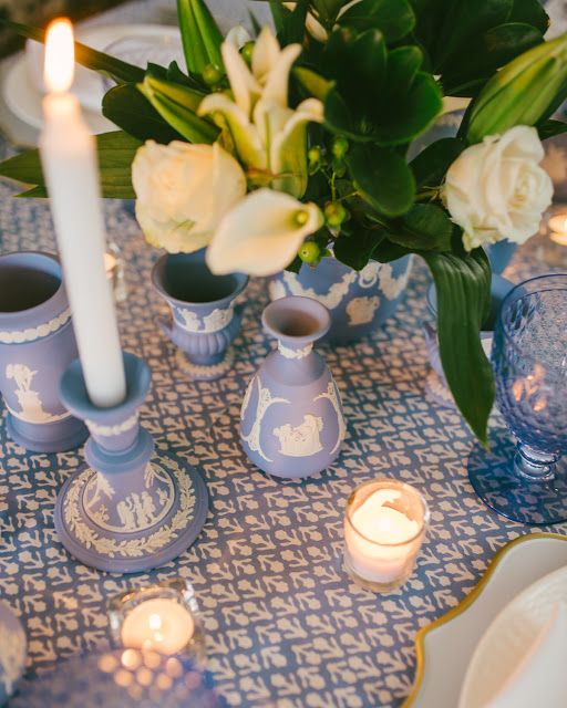 the table is set with blue and white dishes, candles, and flowers in vases