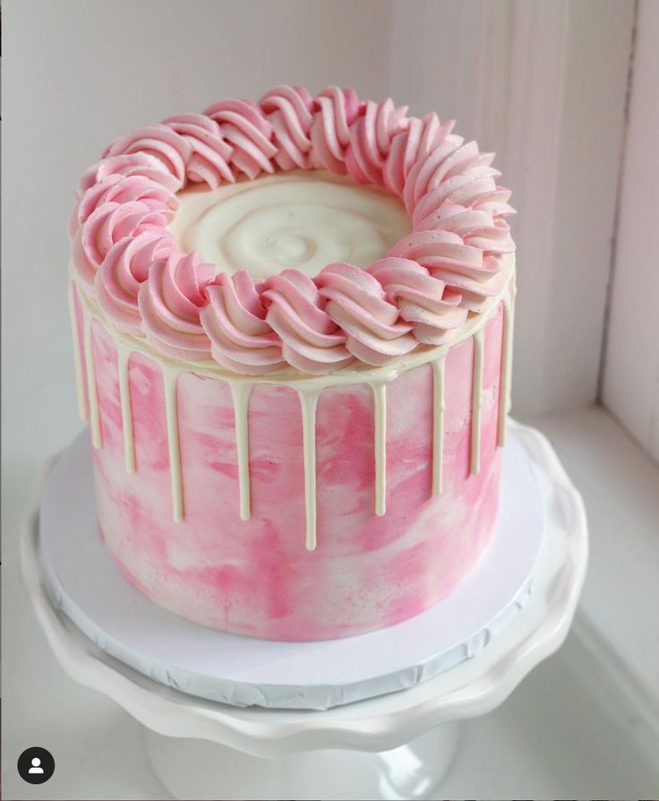 a pink and white cake with icing drizzled around it's edges