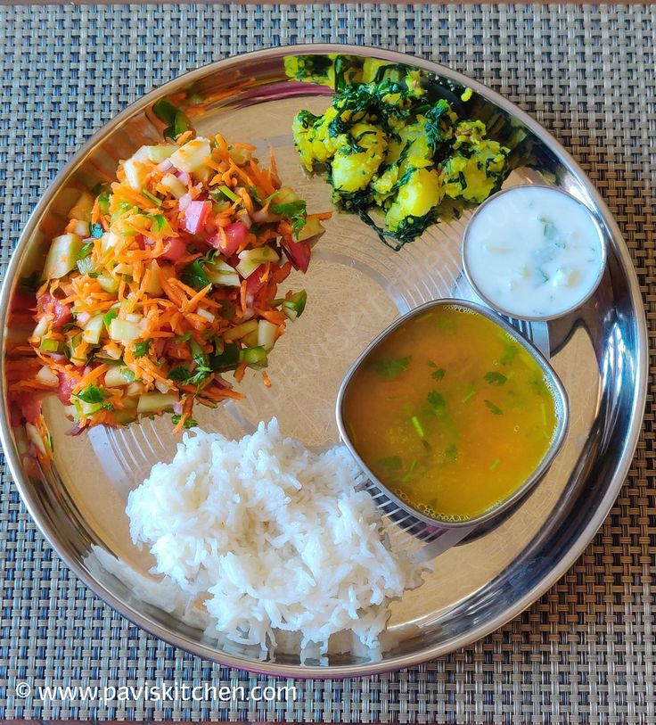 a silver plate topped with rice and veggies next to sauces on a table