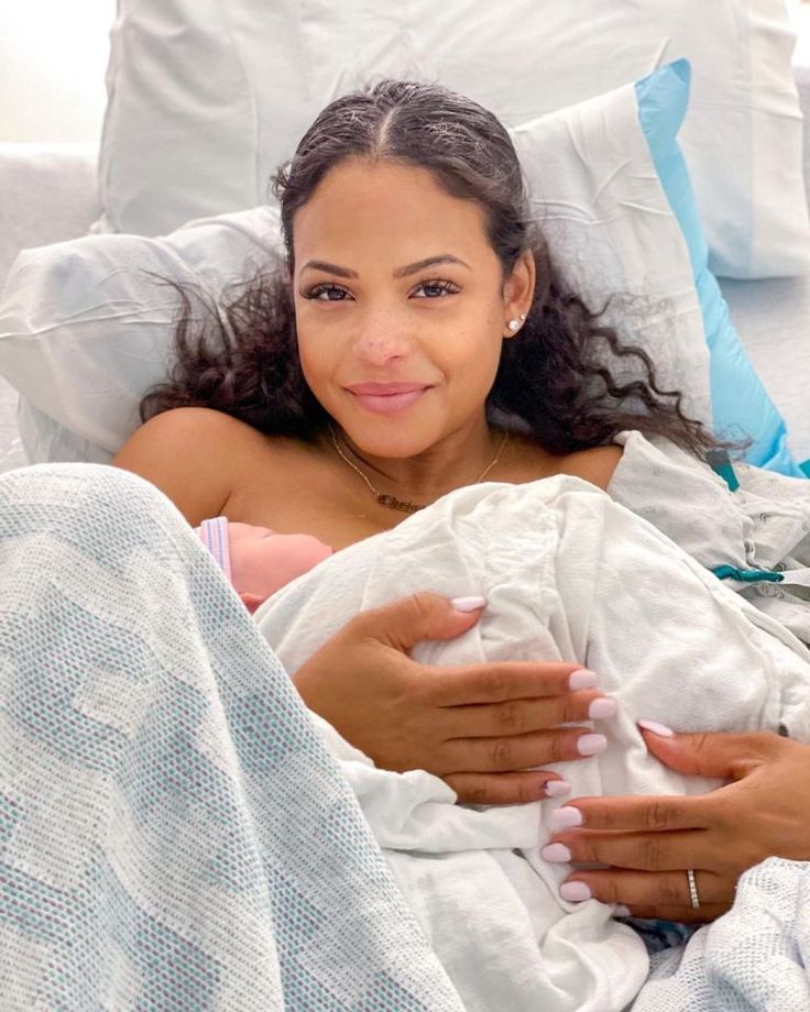 a woman laying in bed holding a baby wrapped in a blanket and smiling at the camera