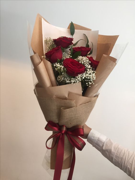 a bouquet of roses wrapped in brown paper and tied with red ribbon is being held by someone's hand