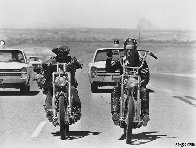 two men riding motorcycles on the road with cars behind them