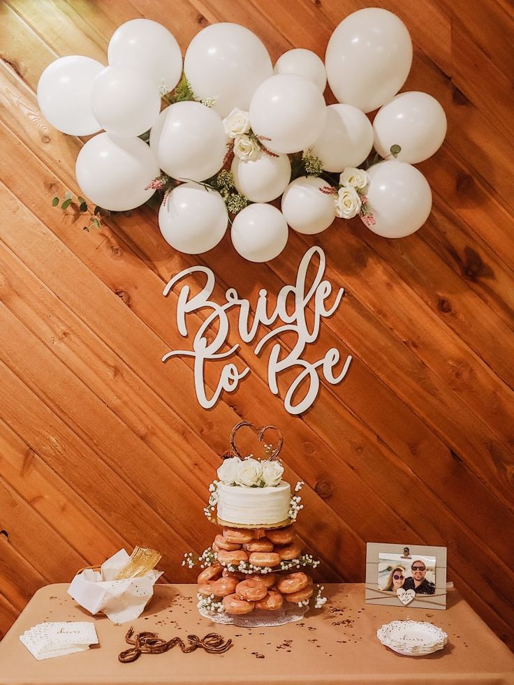 a table topped with a cake covered in frosting next to white balloons and photos