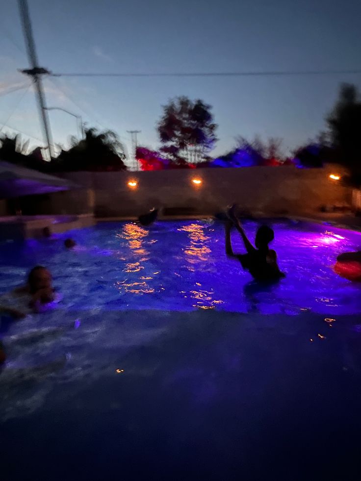 people are in the pool at night with their arms up and one person is swimming