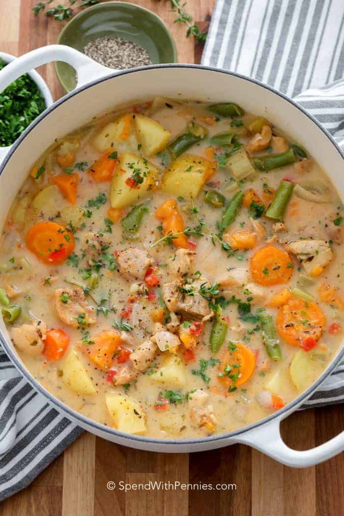 a pot filled with chicken and vegetable soup on top of a wooden table next to other dishes