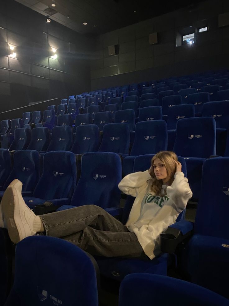 a woman sitting in an empty auditorium with her feet propped up on the seat and looking off to the side