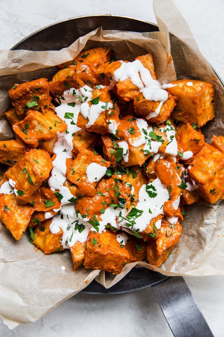 a bowl filled with chicken covered in sauce and parsley on top of a table