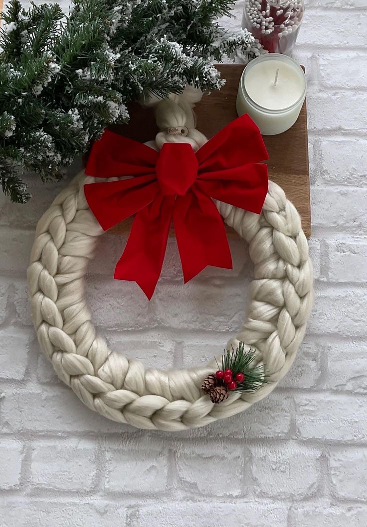 a white rope wreath with a red bow sitting on top of a table next to a candle