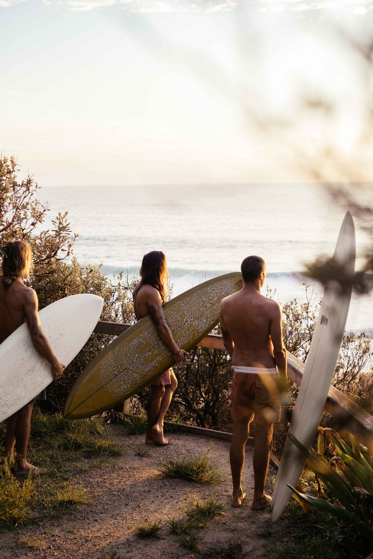 three people carrying surfboards on a path near the ocean