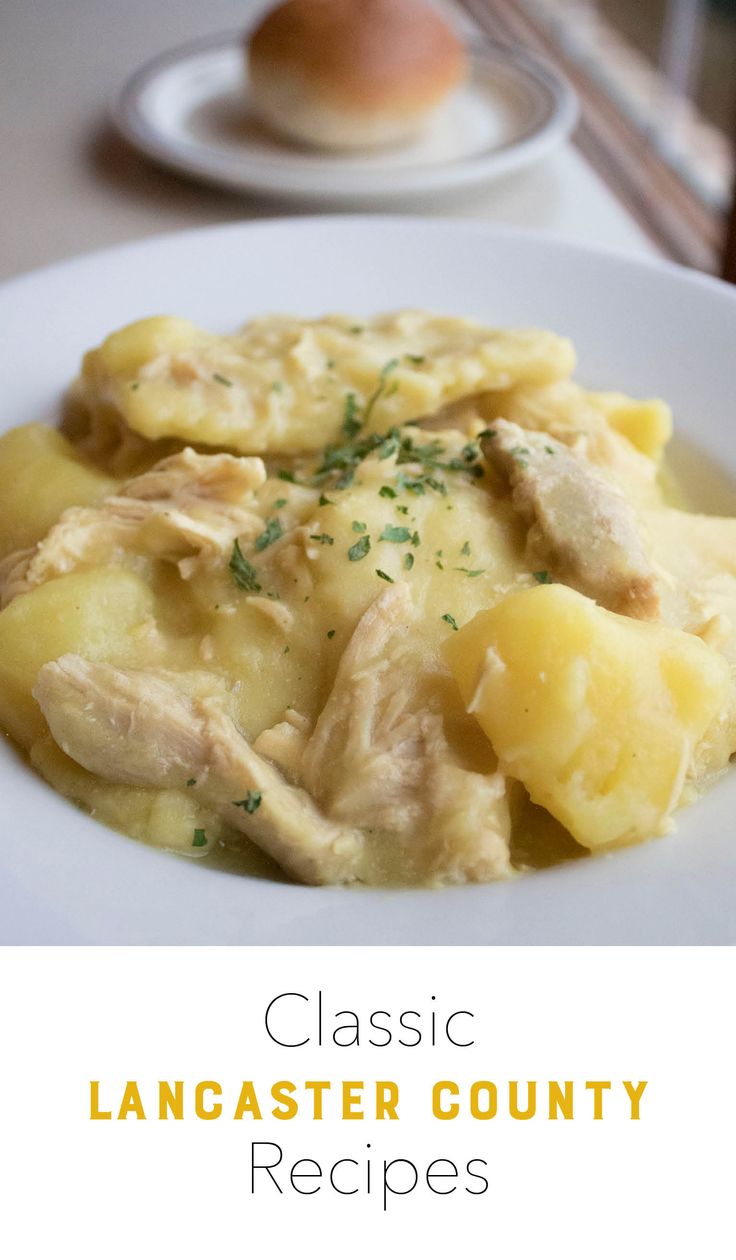 a white plate topped with pasta covered in chicken and cheese next to bread on a table