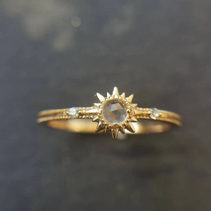 a yellow gold ring with an oval stone and two small diamonds on the band, sitting on a black surface