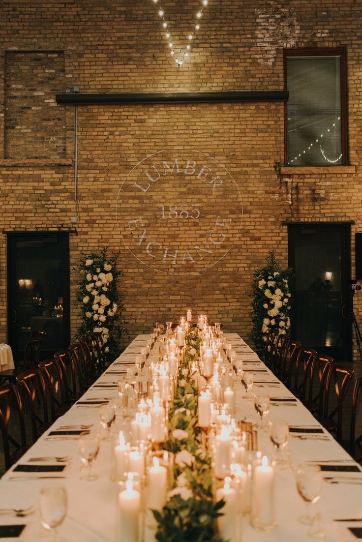 a long table is set with candles and flowers in front of a brick wall that says love