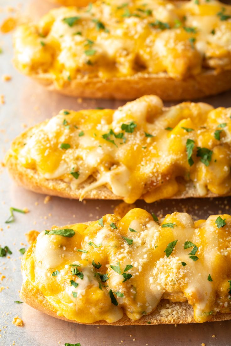 three pieces of bread with cheese and parmesan toppings on them sitting on a baking sheet