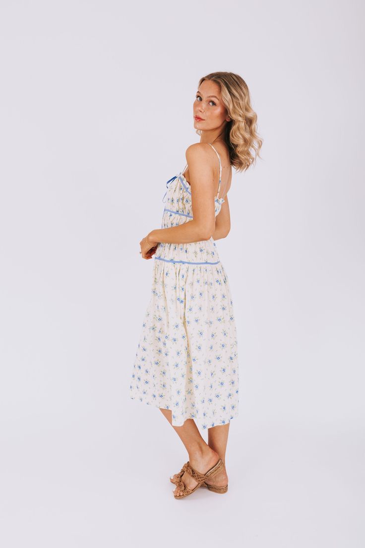 All dressed up and feeling fine, the Cry Baby Dress has got you covered. With adjustable straps and a fully lined design, this dress is as comfortable as it is stylish. The blue floral pattern and piping details add a touch of whimsy, while the front tie and pockets make it both practical and playful. Simply put, it's the perfect combination of fashion and function! Details Adjustable straps Fully lined Blue floral pattern Blue piping details Front tie detail Pockets Sizing Approximate measureme Lined Sundress With Spaghetti Straps For Garden Party, Cotton Floral Print Midi Dress With Spaghetti Straps, Cotton Midi Dress With Floral Print And Spaghetti Straps, Cream Sundress With Spaghetti Straps For Spring, Lined Spaghetti Strap Dress For Daytime, Vacation Midi Dress With Spaghetti Straps And Lining, White Floral Dress With Spaghetti Straps, Daytime Spaghetti Strap Lined Dress, Cream Summer Dress With Adjustable Straps