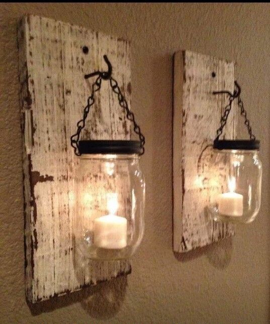 two mason jars are hanging on the wall with candles in them and one is holding a lit candle