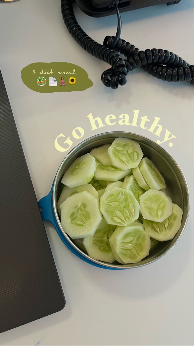 a metal bowl filled with sliced cucumbers on top of a white table next to a laptop