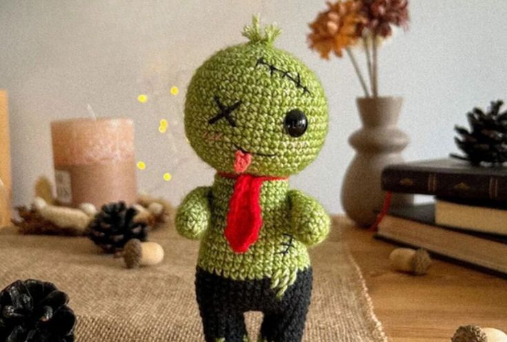 a crocheted zombie doll with a red tie standing in front of some pine cones