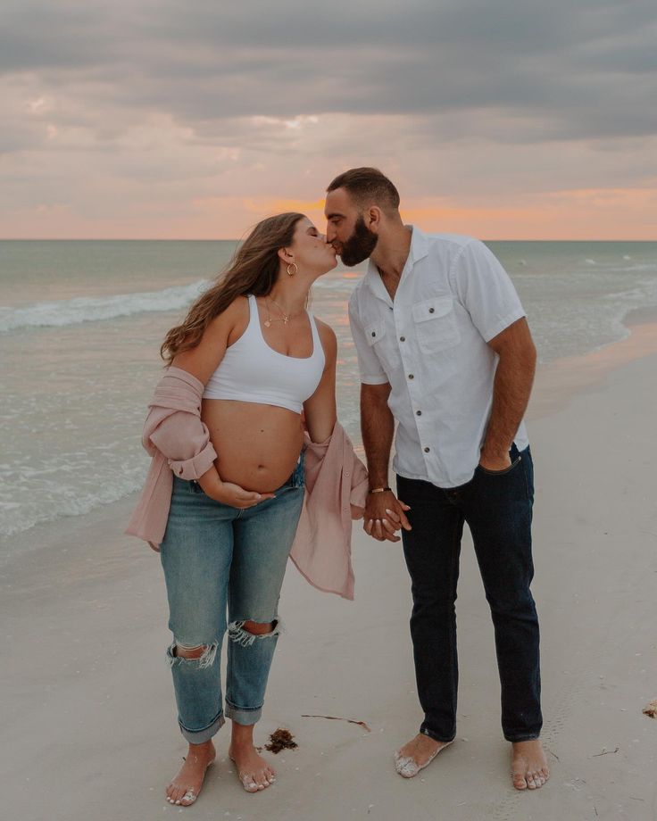 a pregnant couple kissing on the beach at sunset