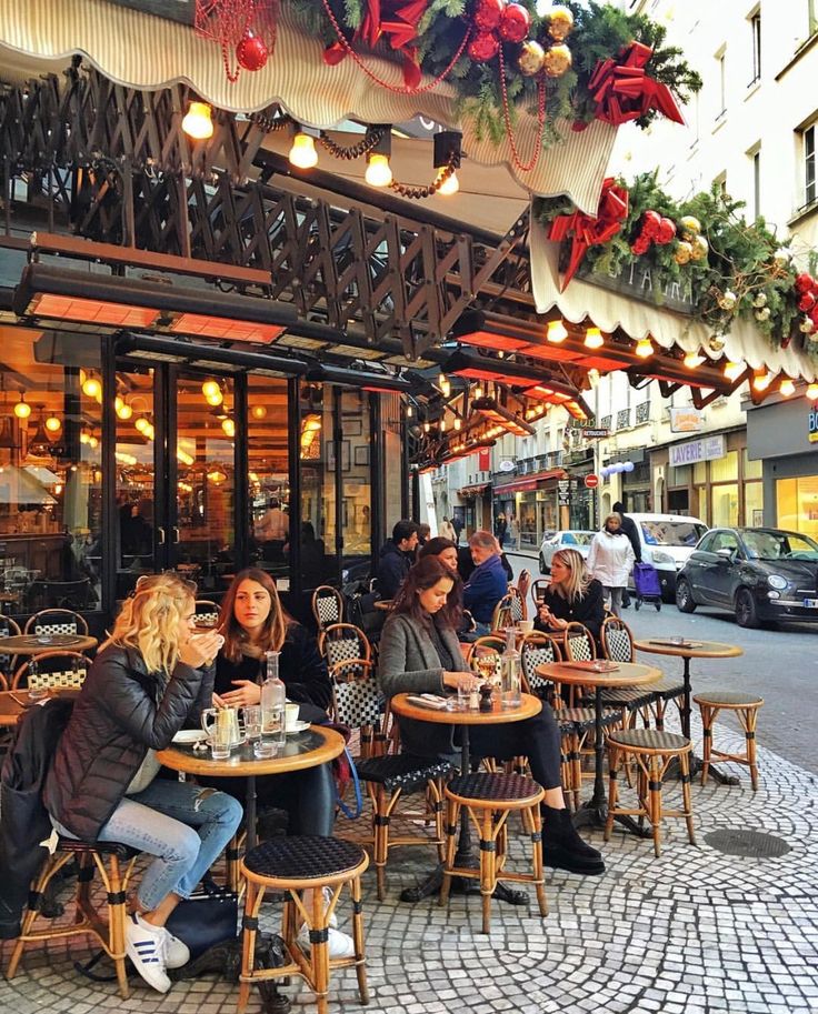 people sitting at tables in front of a building with christmas decorations hanging from the roof