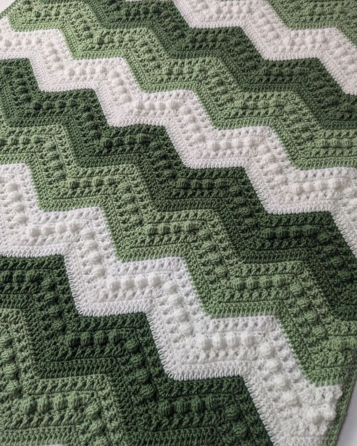 a green and white crocheted blanket on top of a bed