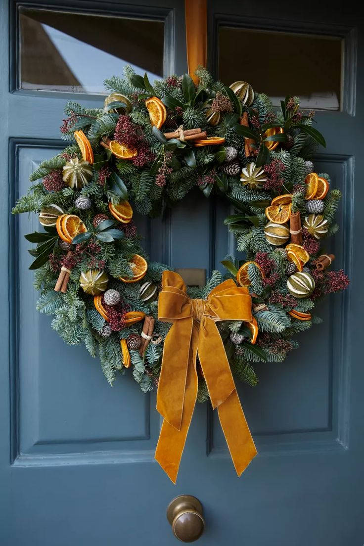 a christmas wreath hanging on a blue door with yellow ribbon and bells attached to it