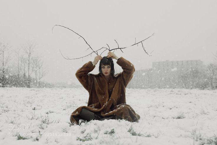 a woman sitting in the snow holding branches above her head