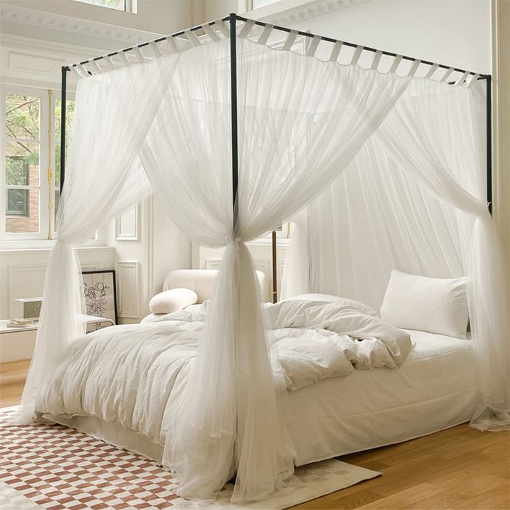 a canopy bed with white sheets and pillows