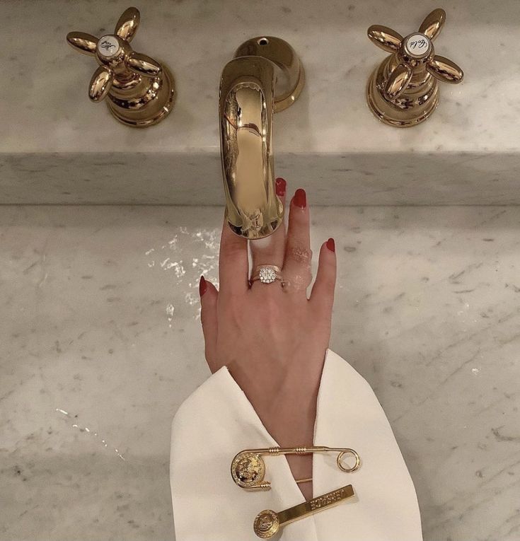 a woman's hand with red nail polish and gold rings in front of a sink