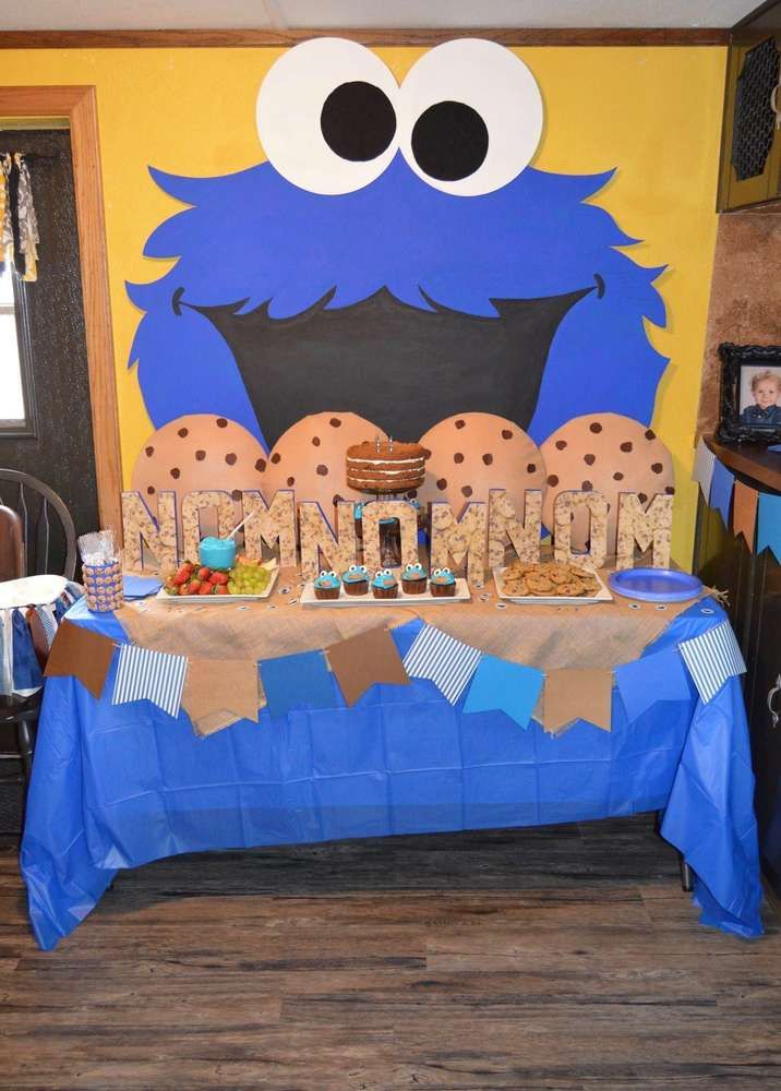 a blue table topped with cookies and cupcakes next to a cookie monster wall