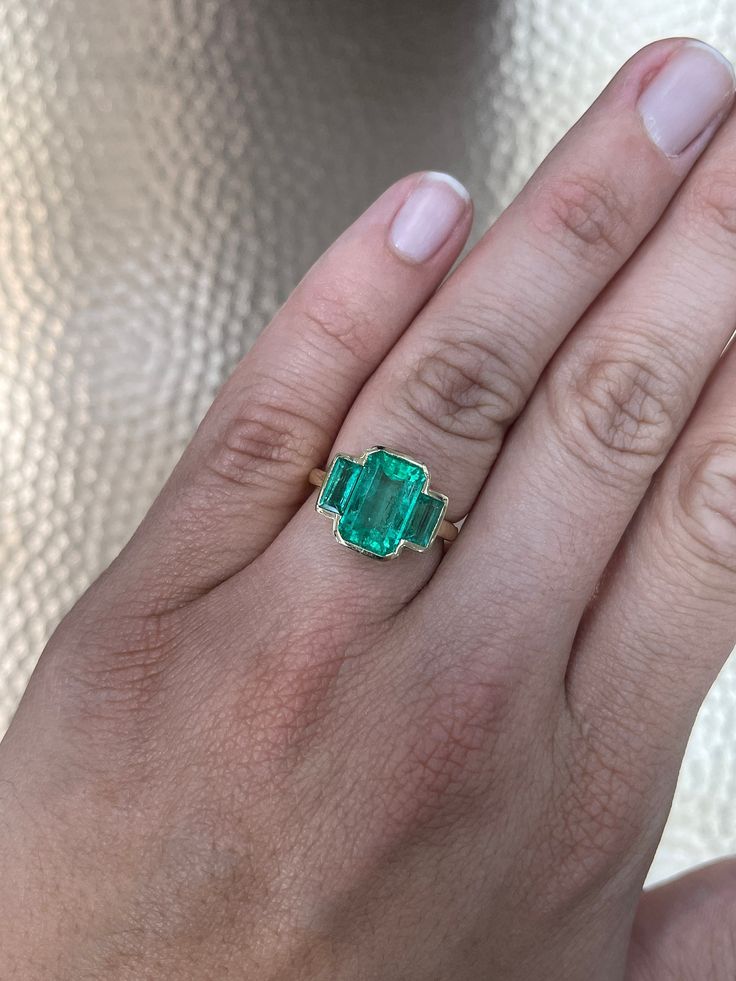 a woman's hand with a green ring on top of her finger and an emerald stone in the middle