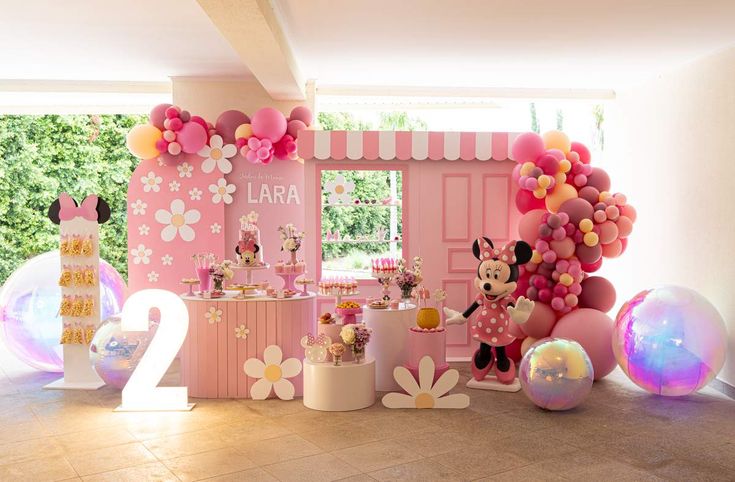 a pink birthday party with balloons and mickey mouse decorations on the wall, along with minnie's first birthday cake