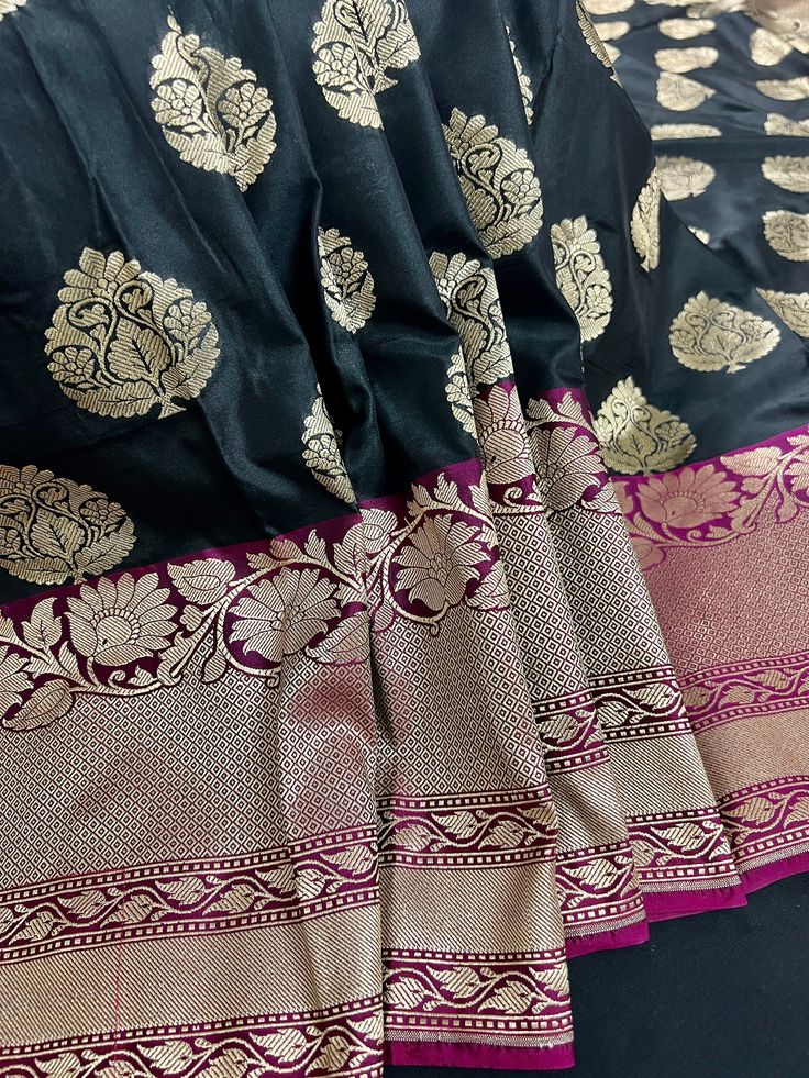 Black Color Banarasi Silk Saree in with Red Borders and Golden Floral Buttas. Item : SareeColor : Black with Dark Pink Borders Base Fabric : Banarasi Soft Silk (Non-Pure)Blouse piece : Comes with Blouse pieceBlouse material : Semi Banarasi SilkWork : Zari Buttas all over the SareeFall & Edging: Comes with Fall and edging (Pico) and tassels attached.Disclaimer -:- Color variation is possible due to various reasons like phone or desktop setting, resolution etc. Please don't hold us responsible. Ou Black Choli With Motifs In Traditional Drape, Black Choli With Traditional Drape And Motifs, Traditional Black Choli With Motifs, Black Diwali Choli With Motifs, Black Anarkali Lehenga With Motifs, Anarkali Black Lehenga With Motifs, Black Bollywood Lehenga With Motifs, Festive Black Choli With Motifs, Festive Black Dola Silk Blouse Piece