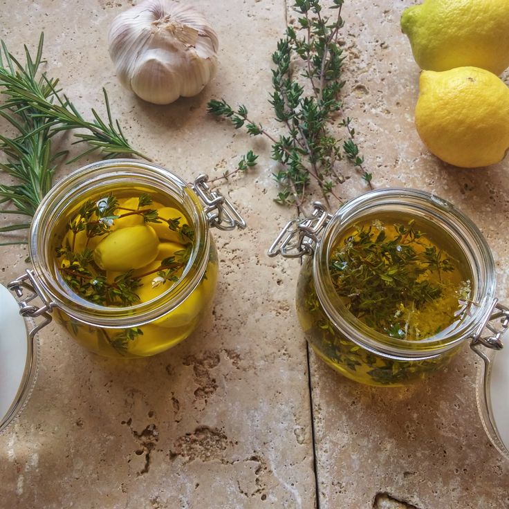 two jars filled with lemons, herbs and garlic on a table next to some lemons