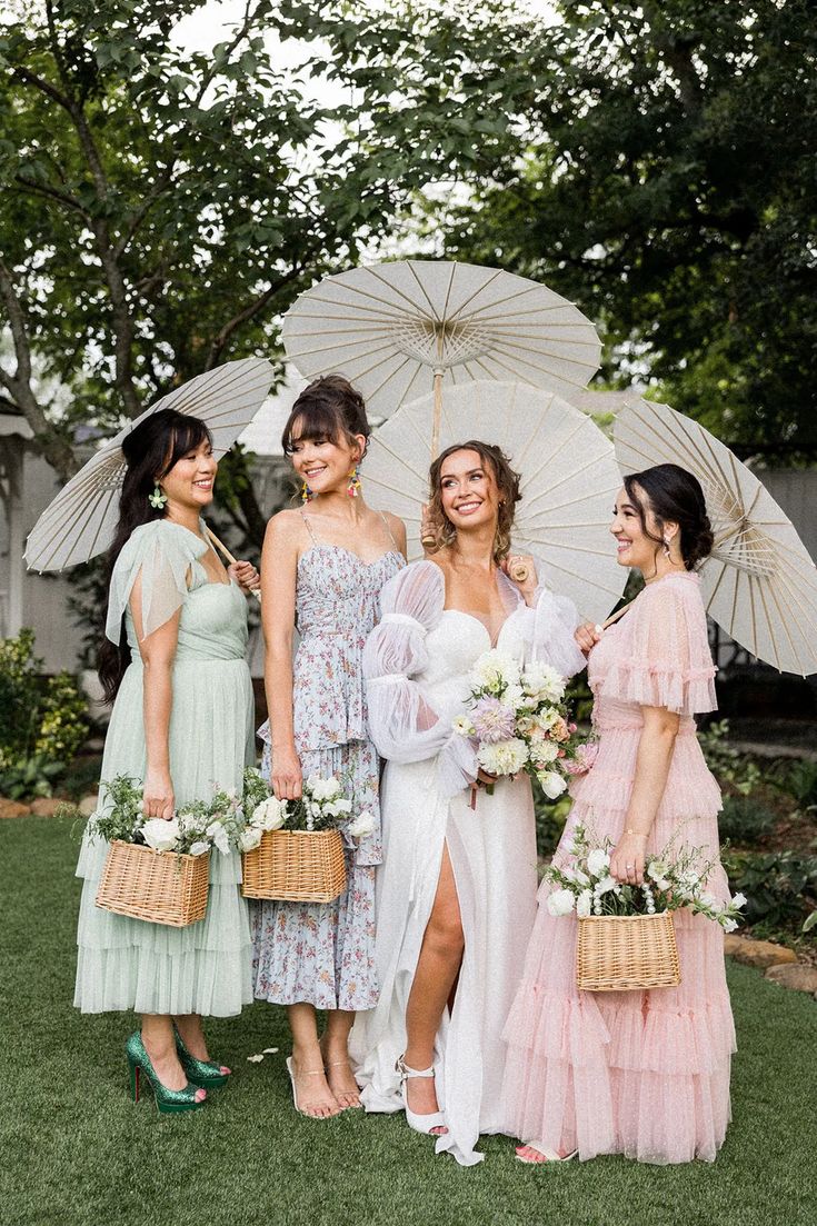 four bridesmaids in pastel dresses holding parasols and flower bouquets