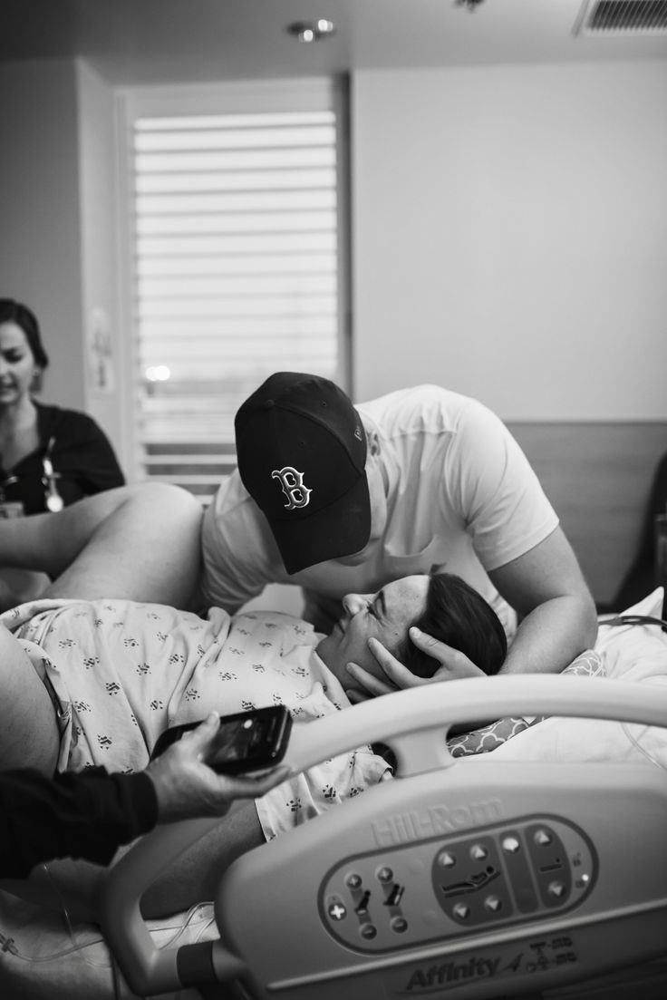 a man in a hospital bed looking at his cell phone while two women look on