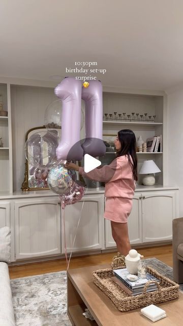 a woman is holding balloons in the shape of two large pink letters, while standing on a coffee table