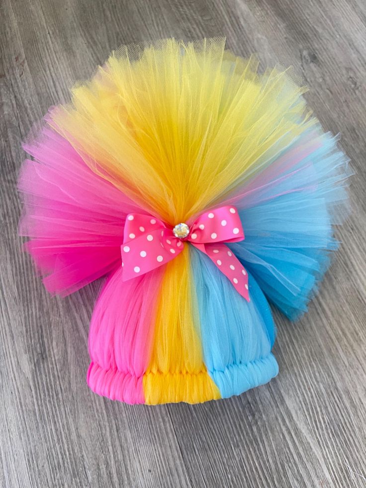 a colorful tutu hat with polka dots and a bow on the top, sitting on a wood floor